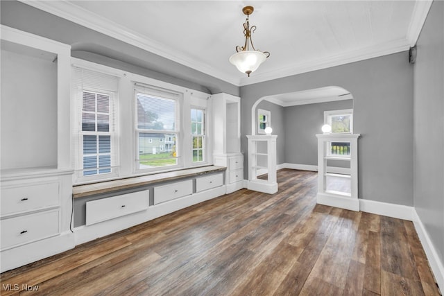 unfurnished dining area featuring arched walkways, dark wood finished floors, crown molding, and baseboards