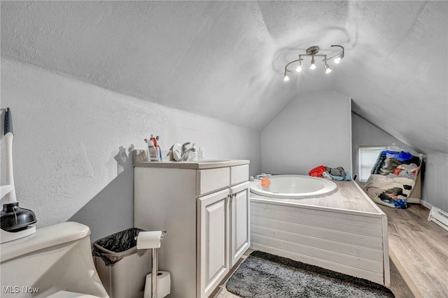 bathroom featuring a textured ceiling, a washtub, hardwood / wood-style floors, toilet, and vaulted ceiling