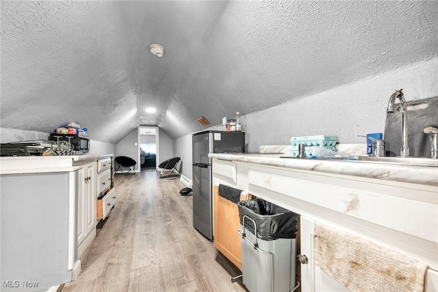additional living space featuring light wood-type flooring, a textured wall, vaulted ceiling, and a textured ceiling