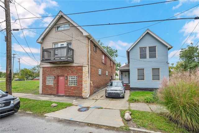 view of front of property with brick siding, a front lawn, and a balcony