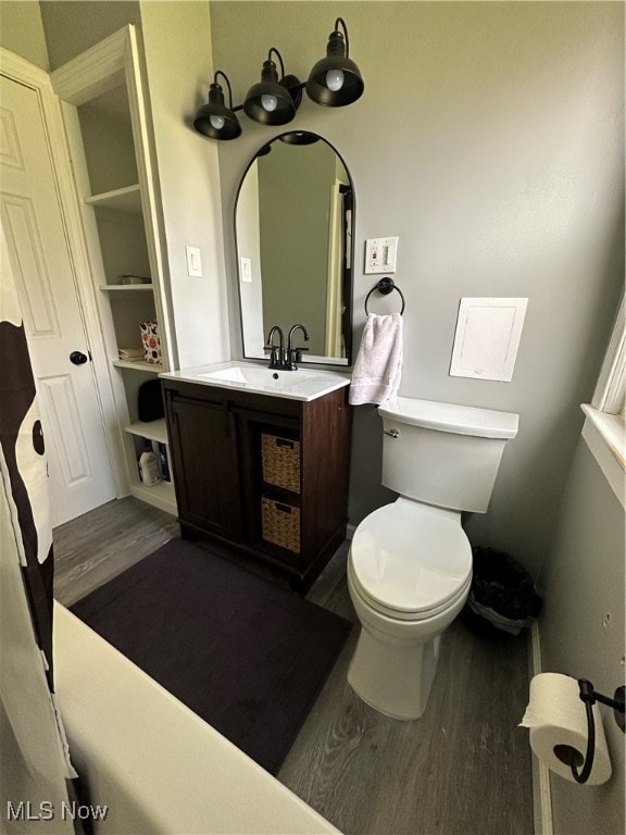 bathroom with built in features, wood-type flooring, vanity, and toilet