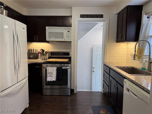 kitchen featuring light stone countertops, dark brown cabinets, white appliances, and sink