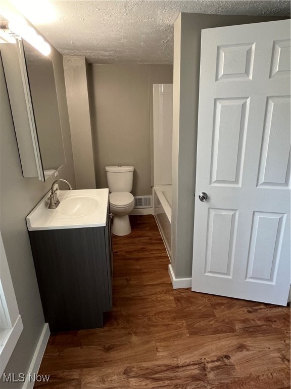 bathroom with vanity, a textured ceiling, hardwood / wood-style flooring, and toilet