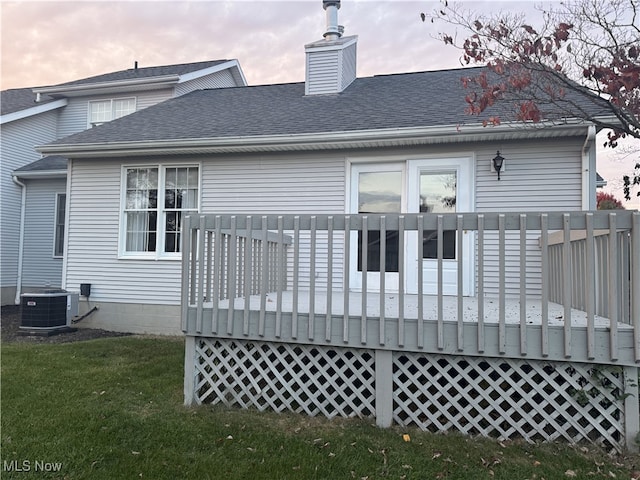 back house at dusk with central air condition unit, a deck, and a yard