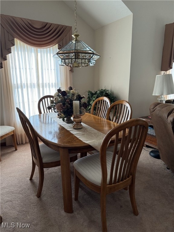 carpeted dining space with a notable chandelier and lofted ceiling