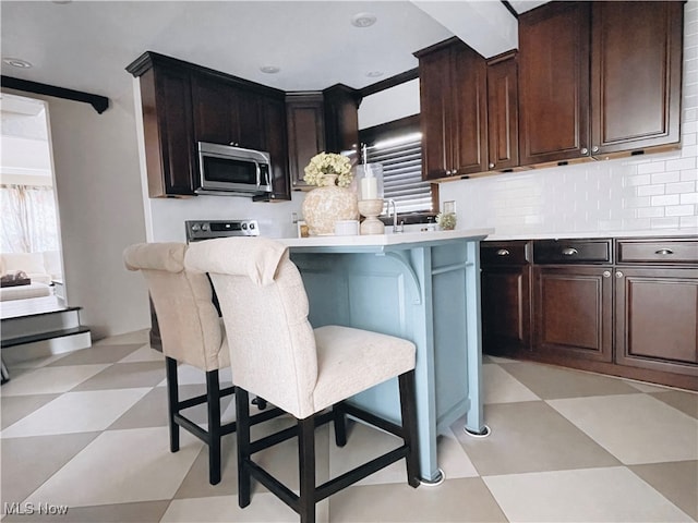 kitchen with a breakfast bar area, appliances with stainless steel finishes, and dark brown cabinets