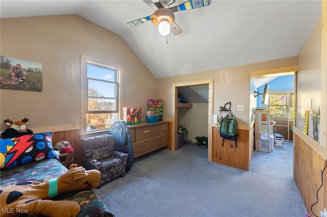 bedroom with lofted ceiling, a closet, wooden walls, light carpet, and ceiling fan