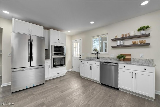 kitchen featuring a sink, light stone countertops, light wood finished floors, and stainless steel appliances