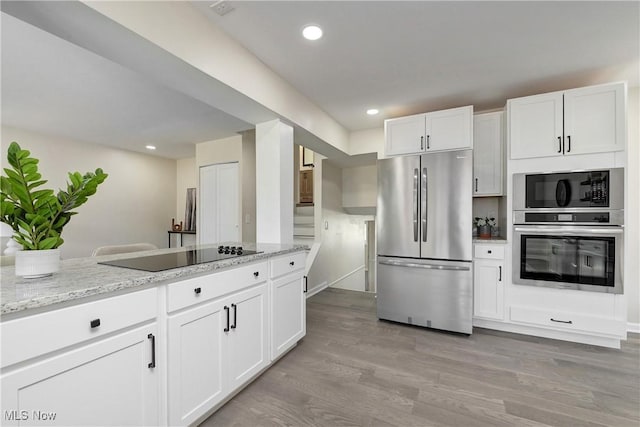 kitchen with light wood finished floors, black appliances, light stone counters, recessed lighting, and white cabinetry