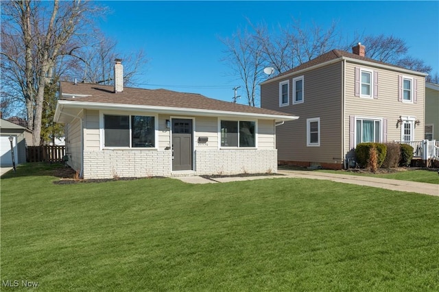 view of front facade with a front yard, fence, a shingled roof, a chimney, and brick siding