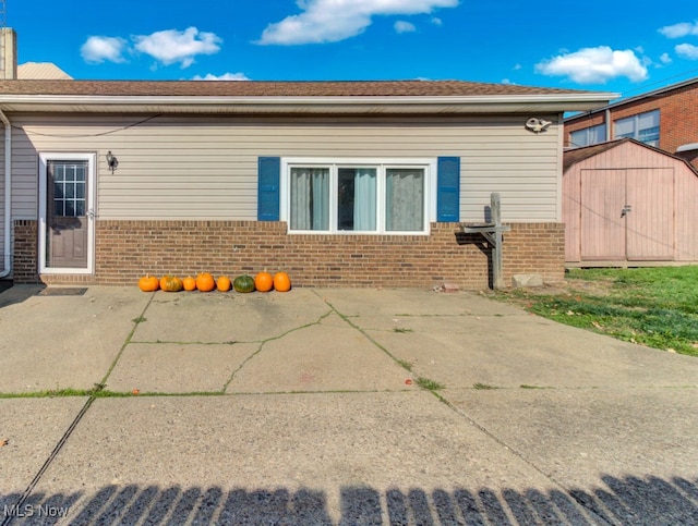 rear view of house featuring a patio area, brick siding, an outdoor structure, and a shed