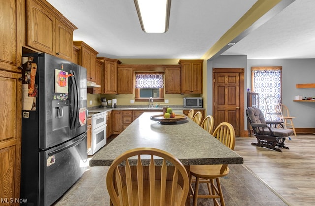 kitchen with appliances with stainless steel finishes, sink, light wood-type flooring, a kitchen island, and a breakfast bar