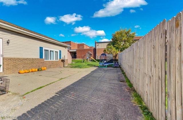 exterior space featuring a patio, a playground, a fenced backyard, brick siding, and a trampoline