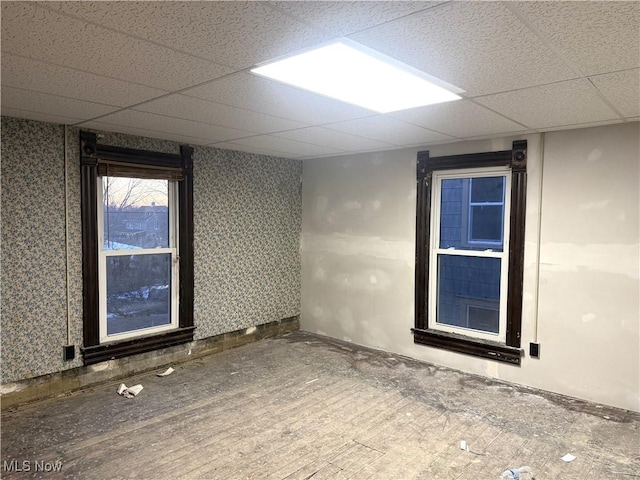 basement featuring a paneled ceiling and wallpapered walls