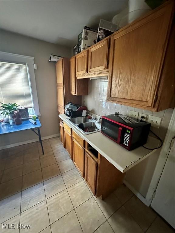 16512 Burnside Ave, Cleveland, OH 44110 - kitchen with brown cabinetry, black microwave, light countertops, tasteful backsplash, and a sink