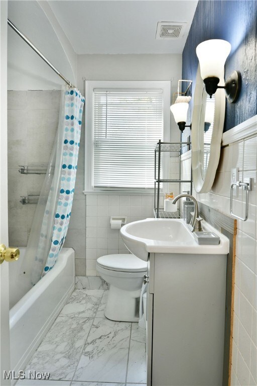 full bathroom with vanity, shower / bath combo, toilet, and tile walls