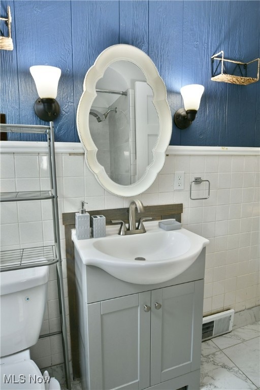 bathroom with toilet, vanity, and tile walls