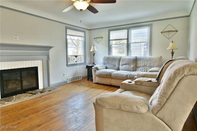 living room with light hardwood / wood-style flooring, ceiling fan, a fireplace, and crown molding