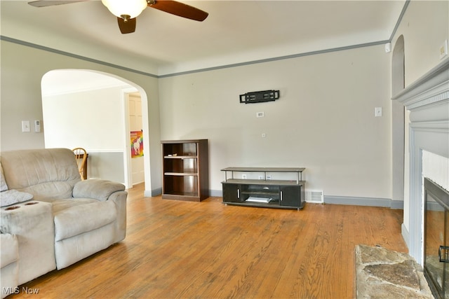 living room with ornamental molding, hardwood / wood-style floors, a stone fireplace, and ceiling fan