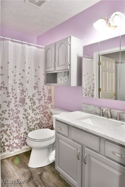 bathroom featuring a textured ceiling, a shower with shower curtain, hardwood / wood-style floors, toilet, and vanity