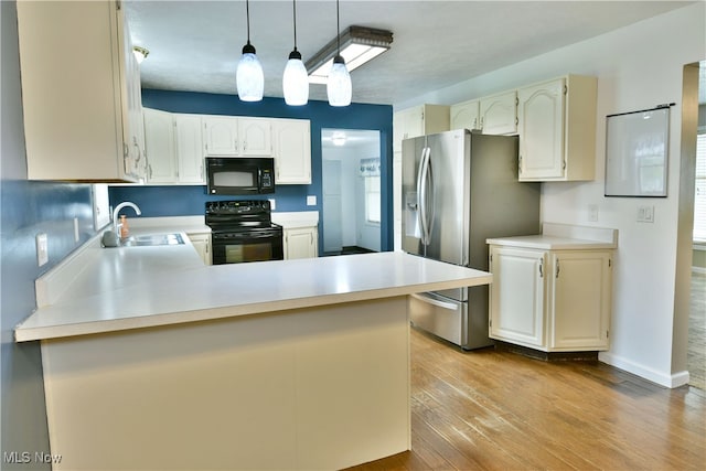 kitchen featuring kitchen peninsula, light wood-type flooring, black appliances, pendant lighting, and sink