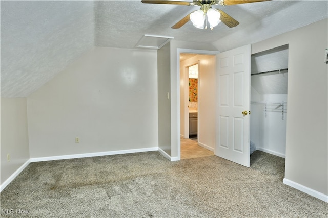 unfurnished bedroom featuring carpet flooring, a textured ceiling, a closet, ceiling fan, and lofted ceiling