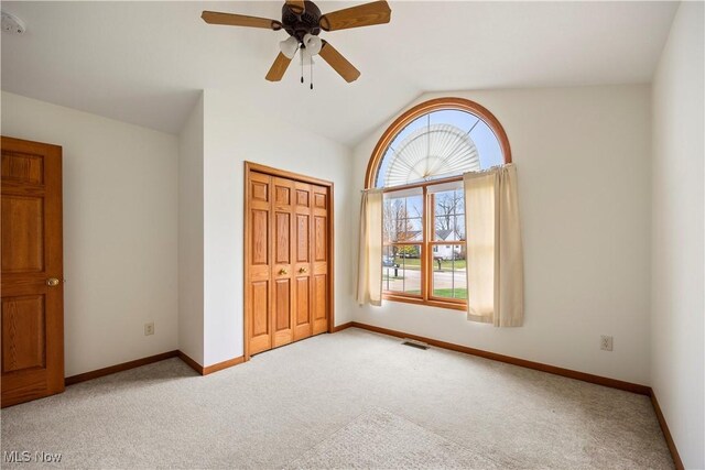 unfurnished bedroom featuring ceiling fan, light colored carpet, a closet, and lofted ceiling