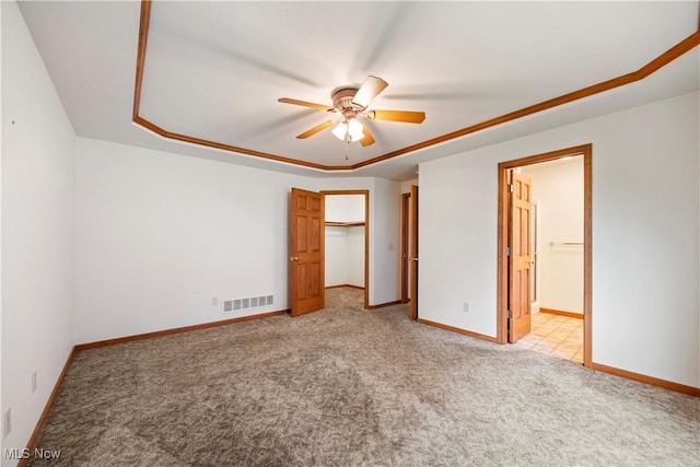 unfurnished bedroom with ceiling fan, light colored carpet, ensuite bath, a raised ceiling, and ornamental molding