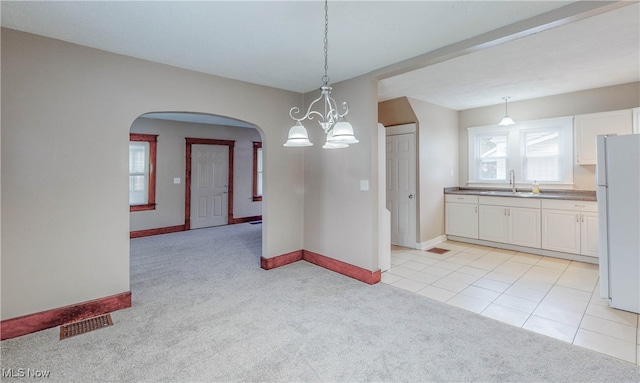 unfurnished dining area featuring sink, a chandelier, and light colored carpet