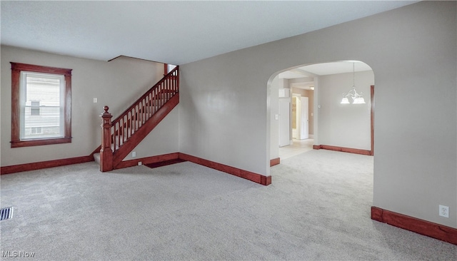 spare room featuring light carpet and an inviting chandelier