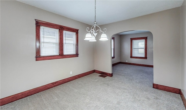 unfurnished room with a notable chandelier, a healthy amount of sunlight, and light carpet