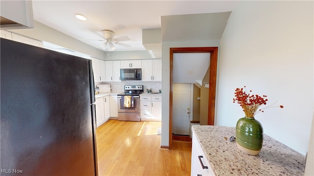 kitchen featuring tasteful backsplash, black appliances, white cabinetry, light hardwood / wood-style floors, and light stone counters