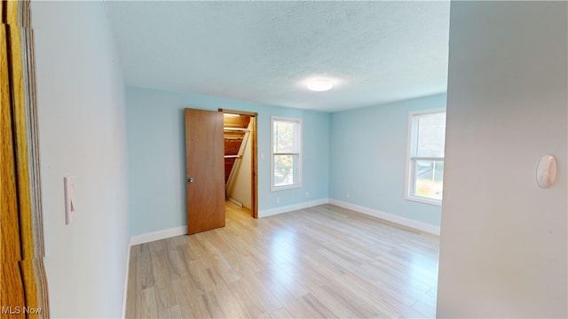 unfurnished bedroom with a spacious closet, a closet, a textured ceiling, and light hardwood / wood-style flooring