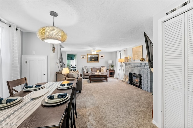 carpeted dining area with a textured ceiling, ceiling fan, a fireplace, and a wealth of natural light