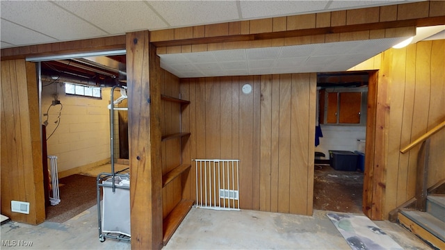 basement with a drop ceiling and wooden walls