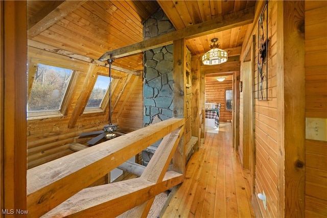 hall featuring light wood-type flooring, lofted ceiling with skylight, rustic walls, and wooden ceiling