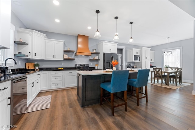 kitchen with custom exhaust hood, white cabinets, hanging light fixtures, sink, and stainless steel appliances