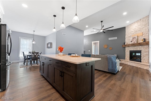 kitchen featuring a stone fireplace, hanging light fixtures, a center island, stainless steel refrigerator, and dark hardwood / wood-style flooring