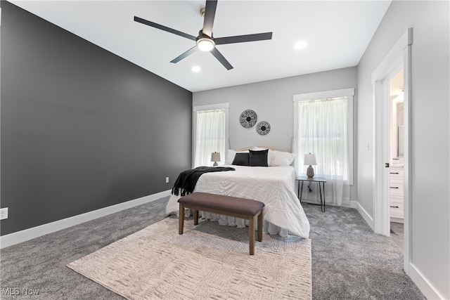 carpeted bedroom with ensuite bath, multiple windows, and ceiling fan