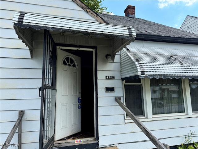 entrance to property featuring roof with shingles and a chimney