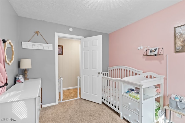 bedroom with light carpet, a nursery area, and a textured ceiling