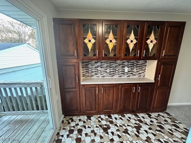 bar with dark brown cabinets, decorative backsplash, and ornamental molding