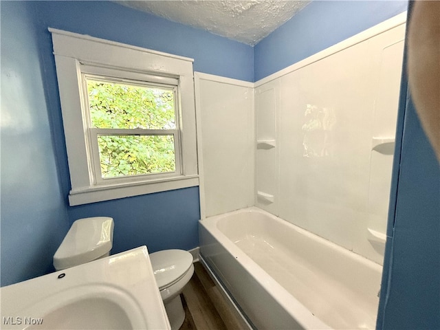 full bathroom with hardwood / wood-style floors, a textured ceiling, toilet, sink, and bathing tub / shower combination