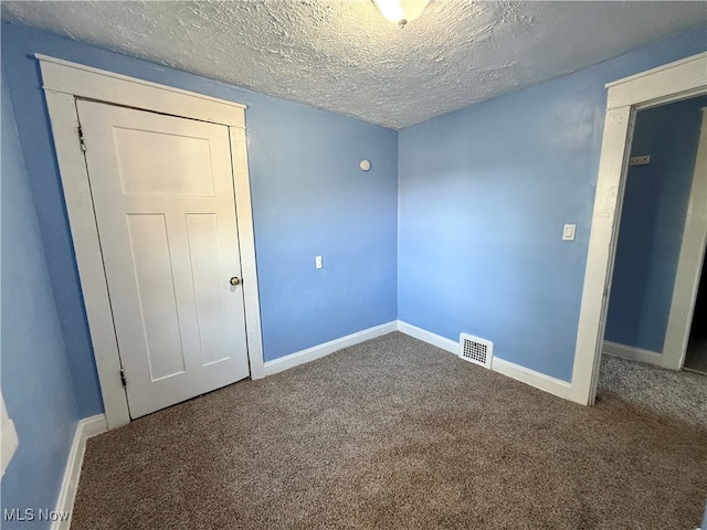 empty room with a textured ceiling and dark colored carpet