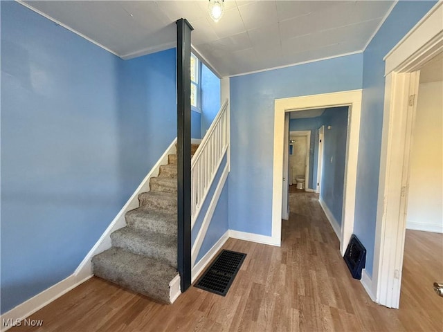 stairway featuring baseboards, visible vents, ornamental molding, and wood finished floors