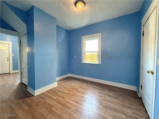 empty room with lofted ceiling, a textured ceiling, and hardwood / wood-style flooring