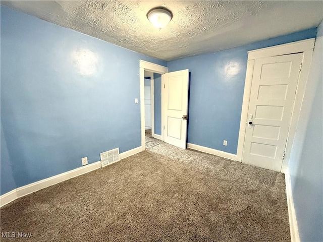 spare room featuring carpet flooring, a textured ceiling, visible vents, and baseboards