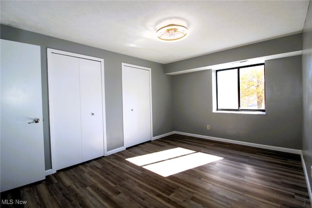 unfurnished bedroom with multiple closets and dark wood-type flooring