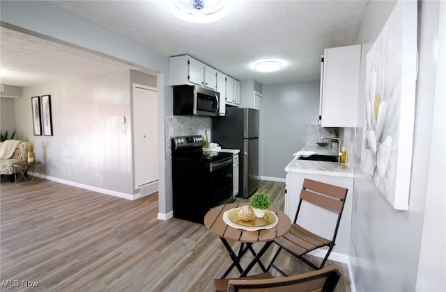 kitchen featuring decorative backsplash, appliances with stainless steel finishes, white cabinetry, light hardwood / wood-style floors, and sink