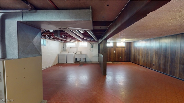 basement featuring sink, wooden walls, washer and clothes dryer, and heating unit